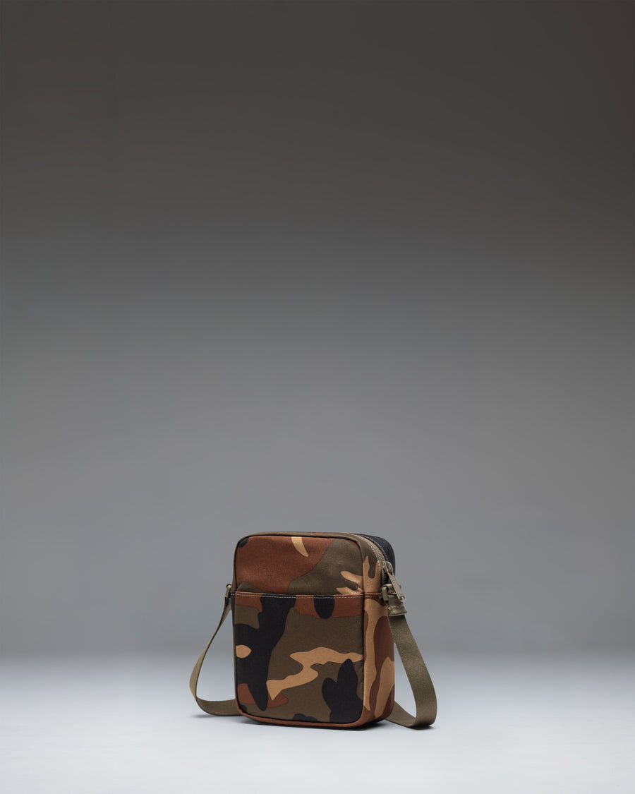 Herschel Heritage Crossbody bag in Woodland Camo with a black label, showing the front view with zipper detail.