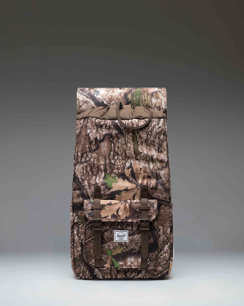 Herschel Little America Backpack in Realtree APX Camo pattern, featuring a classic mountaineering design with dual magnetic strap closures.