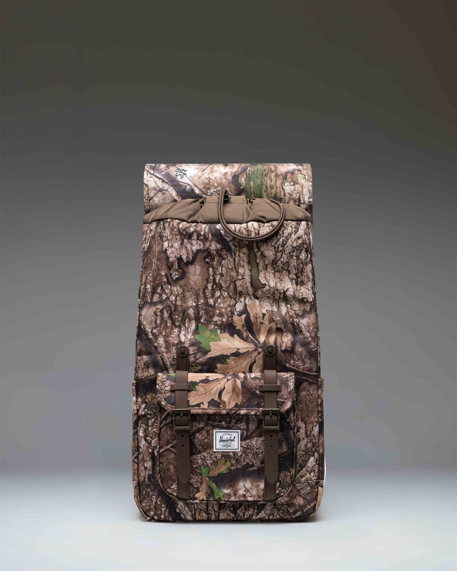 Herschel Little America Backpack in Realtree APX Camo pattern, featuring a classic mountaineering design with dual magnetic strap closures.