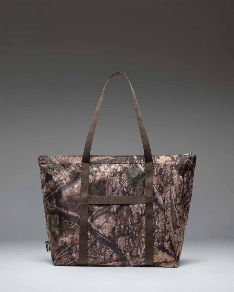 Herschel Supply Co. Realtree Portland Packable Tote in Realtree APX Camo pattern, showing a close-up lifestyle view of the durable fabric.