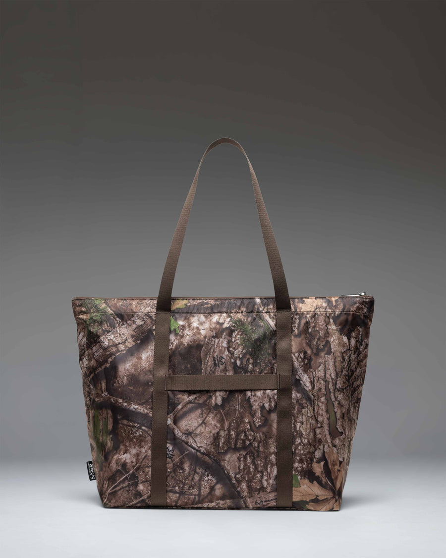Herschel Supply Co. Realtree Portland Packable Tote in Realtree APX Camo pattern, showing a close-up lifestyle view of the durable fabric.