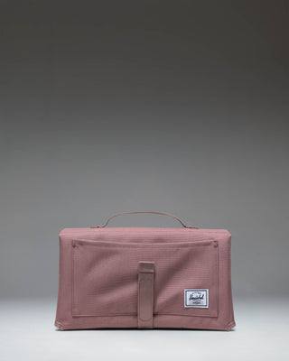 Herschel Supply Co Sprout Change Mat in Ash Rose pink, folded up and secured with a strap.