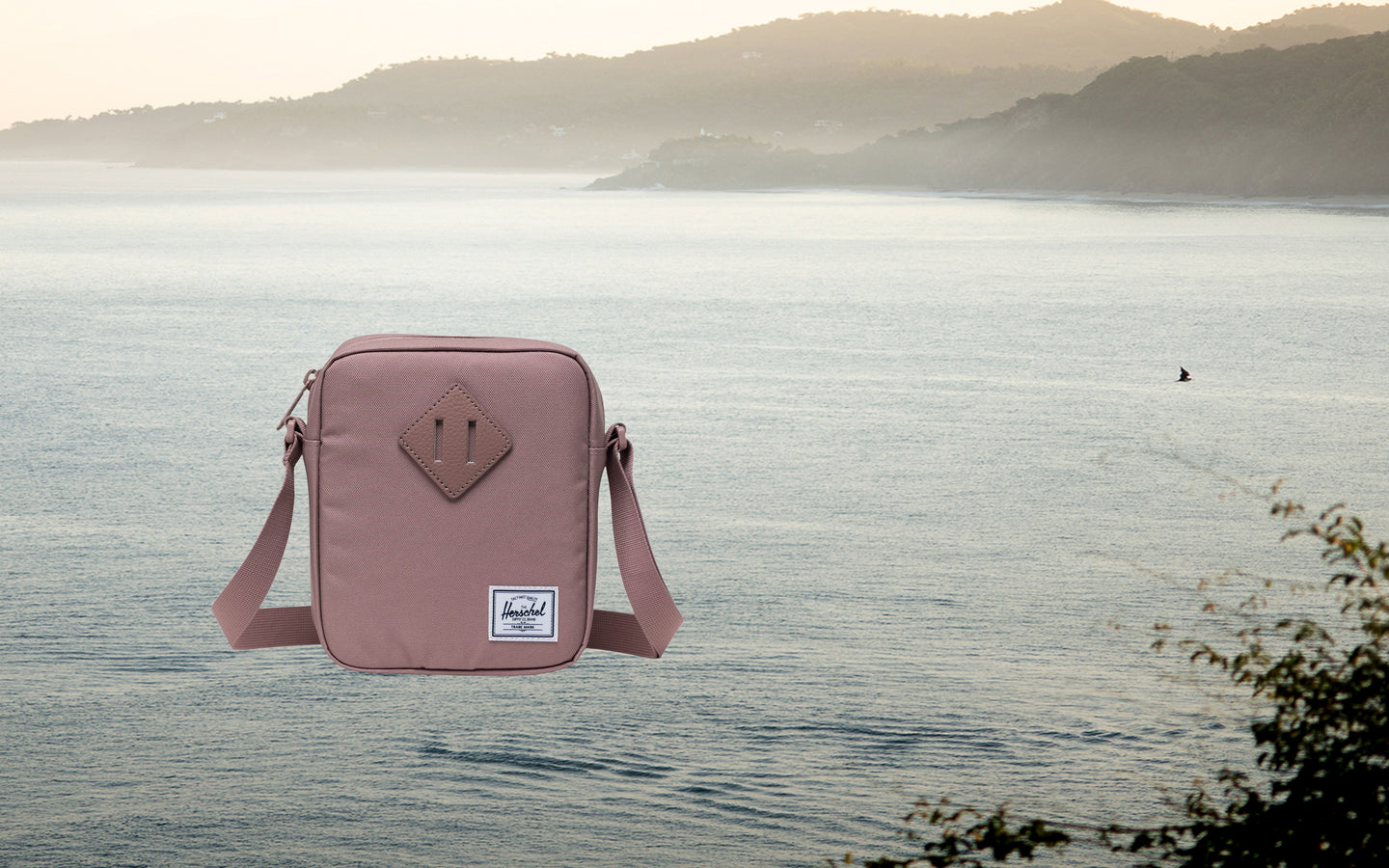 Herschel Supply Co. Herschel Heritage Crossbody bag in Ash Rose, lifestyle view on a desktop background.