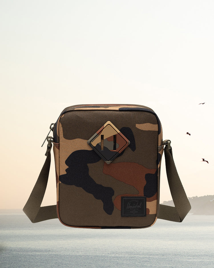 Herschel Heritage Crossbody bag in Woodland Camo with a Black Label, shown on a mobile lifestyle model.