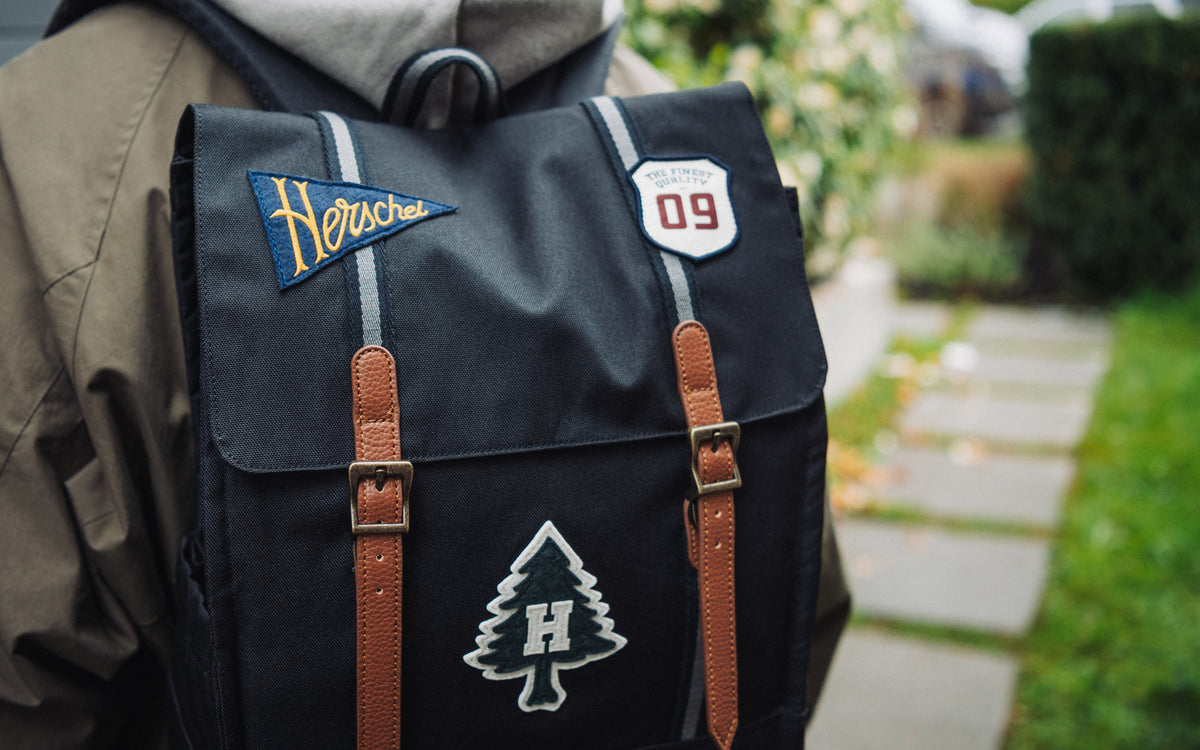 Herschel Survey Backpack in Patches Black featuring a black body with assorted colorful patches sewn onto the front.