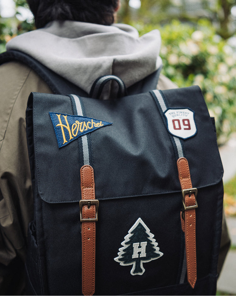Herschel Survey Backpack in Patches Black, showing a clean, modern design with dual straps and a front pocket.