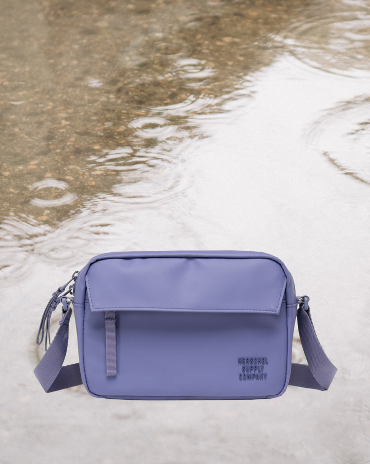 Herschel Supply Co. Alberni Crossbody bag in Heron grey, showing a front view on a mobile display layout.