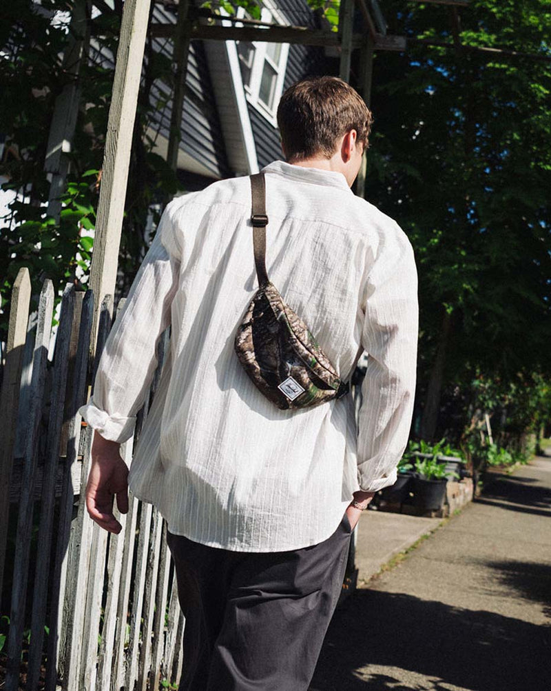Herschel Classic Hip Pack in Realtree APX Camo pattern on a mobile screen lifestyle view.