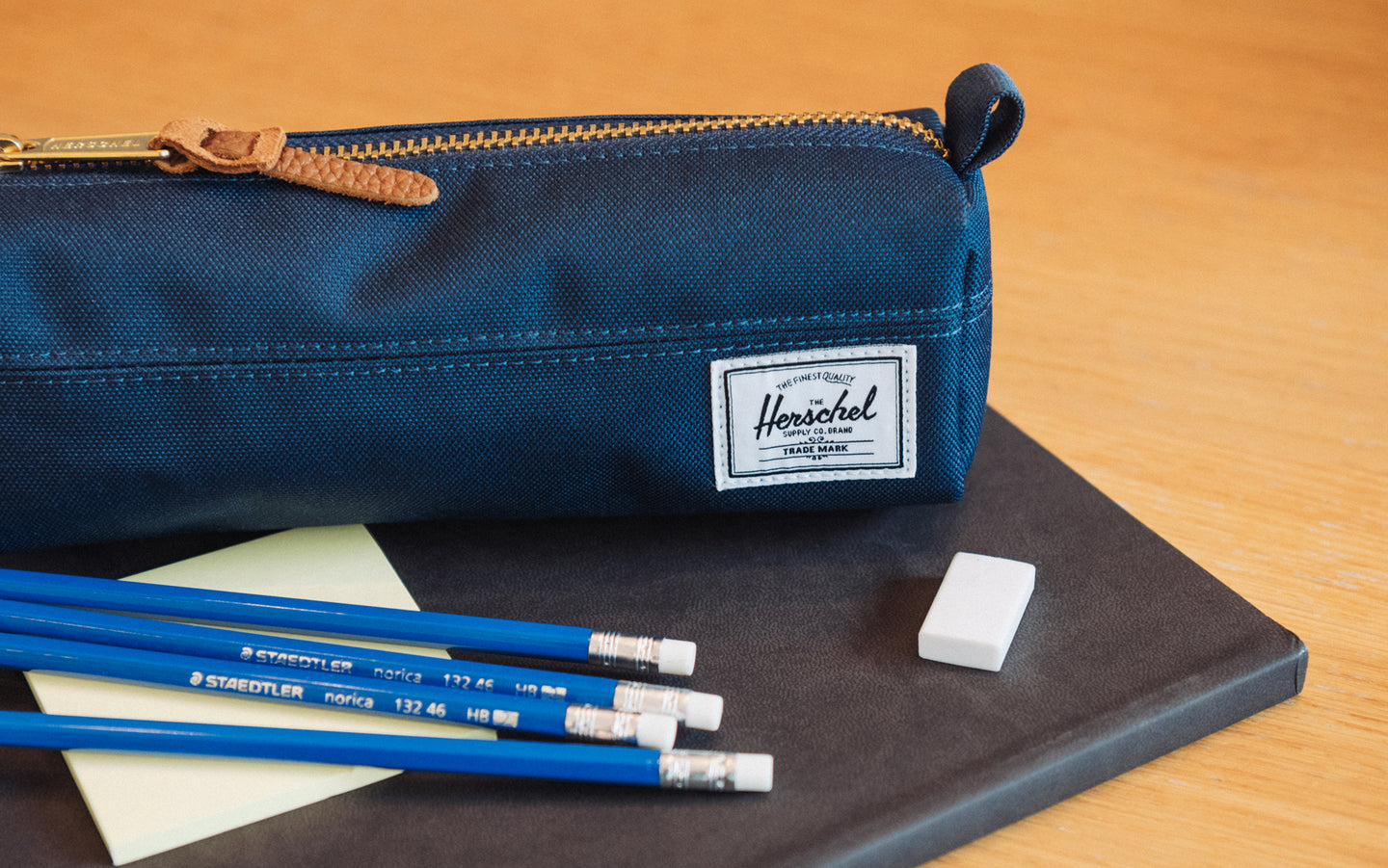 Navy Herschel Settlement Pencil Case shown from a side profile view, featuring a exposed gold-tone zipper and a classic woven label.