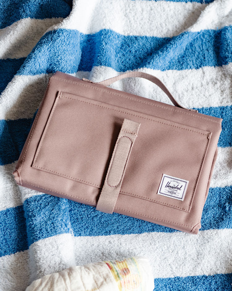 Herschel Supply Co. Sprout Change Mat in Ash Rose pink unfolded and laid flat, showing the padded surface and signature striped liner.
