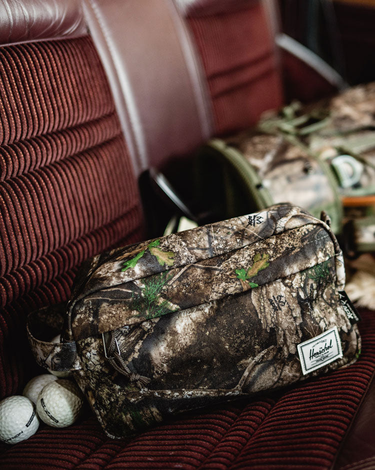 Herschel Supply Co. Chapter Travel Kit in Realtree APX Camo, featuring a side handle and front zippered pocket.