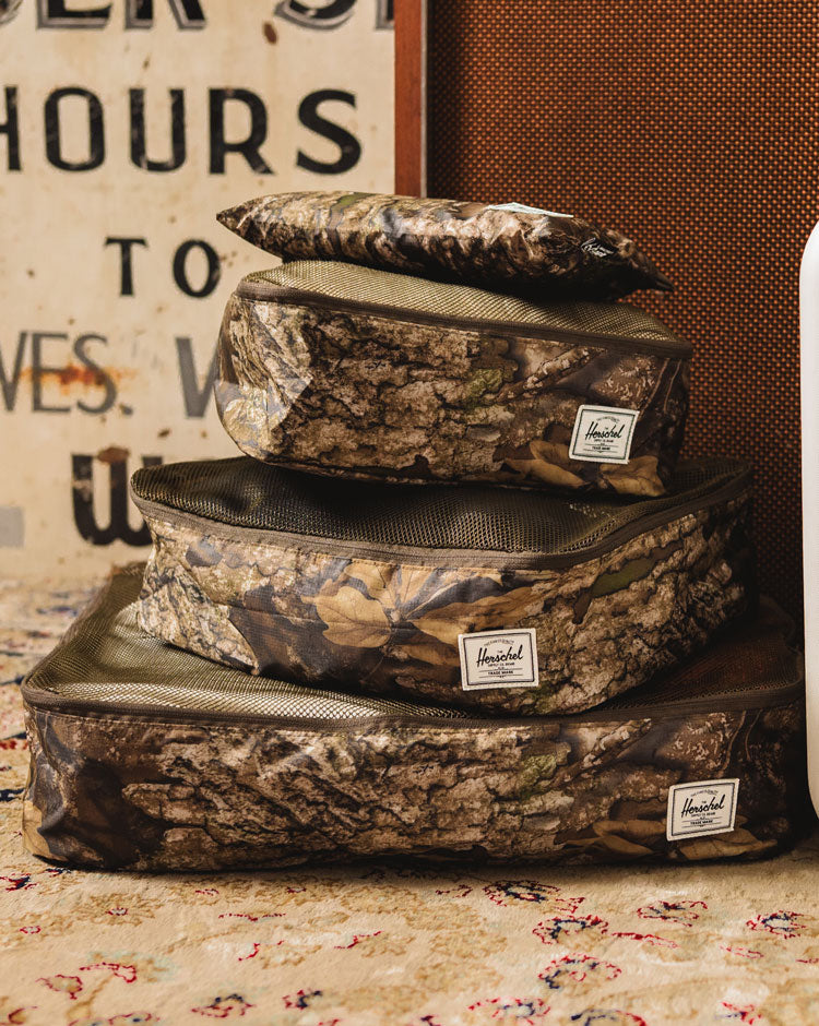 Herschel Supply Co Realtree Kyoto Packing Cubes in Realtree APX Camo shown in a set of three organized inside an open travel bag.