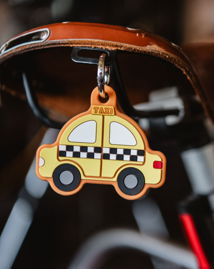 Yellow silicone bag charm shaped like a classic New York City taxi with black and white checkered patterns and a metal keyring.