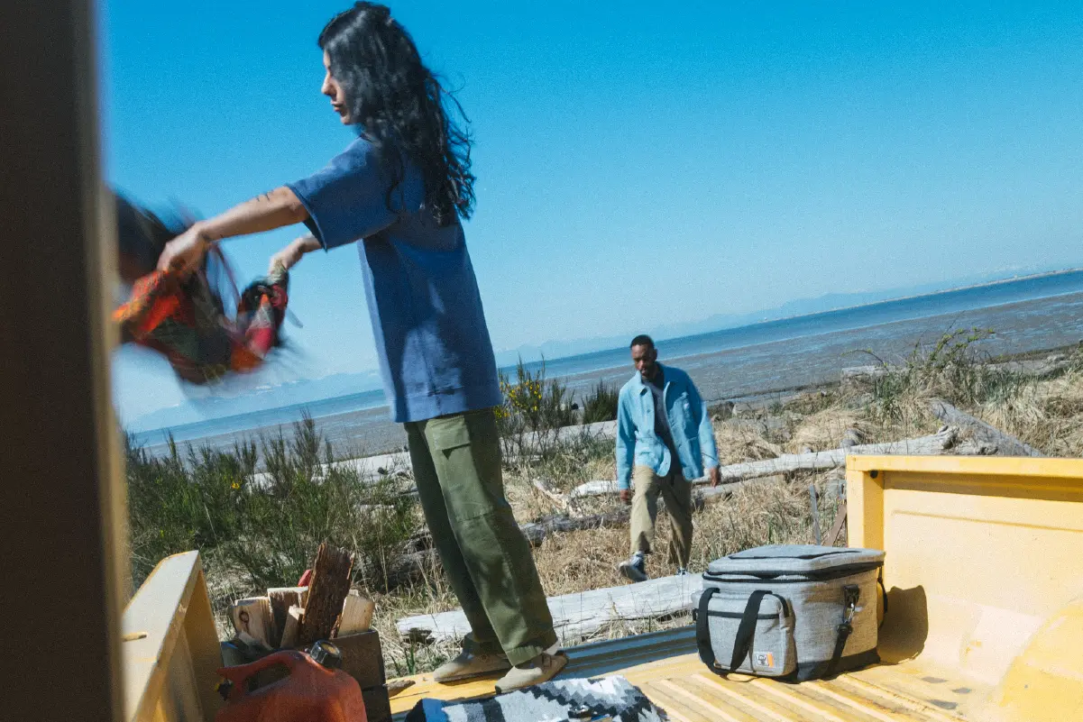 A person unloading supplies out of the back of a pick-up truck with a Herschel Pop Quiz Cooler 30 Pack Insulated behind them.