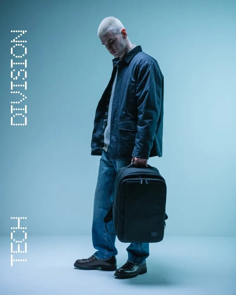 A photo of a Herschel Little America® Backpack in the new seasonal color, Eucalyptus, on a wooden chair with a soft beige backdrop and some eucalyptus leaves on the chair beside it.